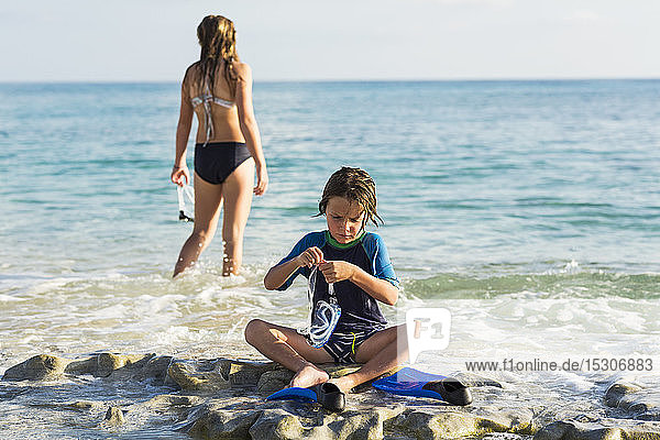 5 Jahre alter Junge beim Anlegen seiner Schwimmflossen am Strand