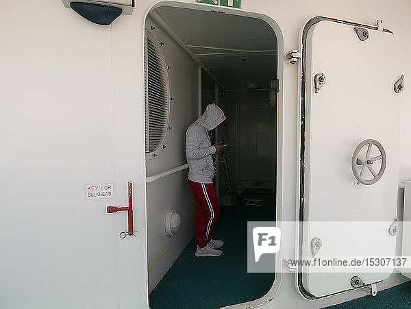Junger Mann mit Smartphone in der Tür auf einem Kreuzfahrtschiff
