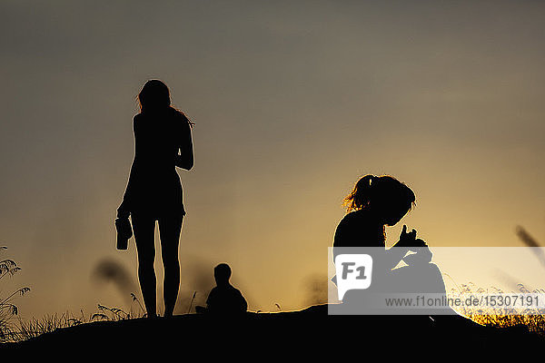 Silhouette Frauen essen und trinken auf einem Hügel bei Sonnenuntergang