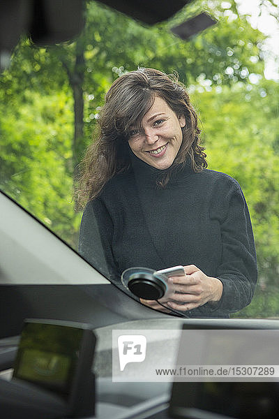 Portrait smiling young woman with smart phone accessing car share