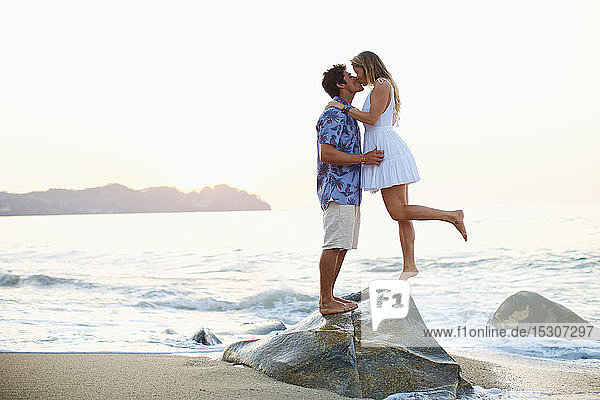 Zärtliches  romantisches junges Paar  das sich auf einem Felsen am Meer küsst  Sayulita  Nayarit  Mexiko