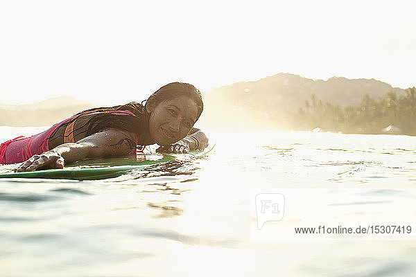 Porträt einer selbstbewussten  gelassenen Surferin  die auf einem Surfbrett im sonnigen Meer liegt