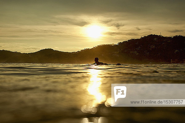 Silhouette young man laying on surfboard on tranquil sunset ocean  Sayulita  Nayarit  Mexico