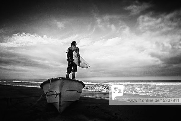 Männlicher Surfer mit Surfbrett auf einem gestrandeten Boot  Higuera Blanca  Nayarit  Mexiko