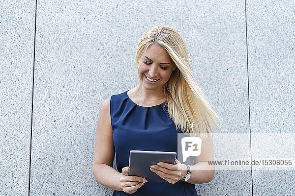 Porträt einer lächelnden blonden Geschäftsfrau  die auf ein digitales Tablet schaut