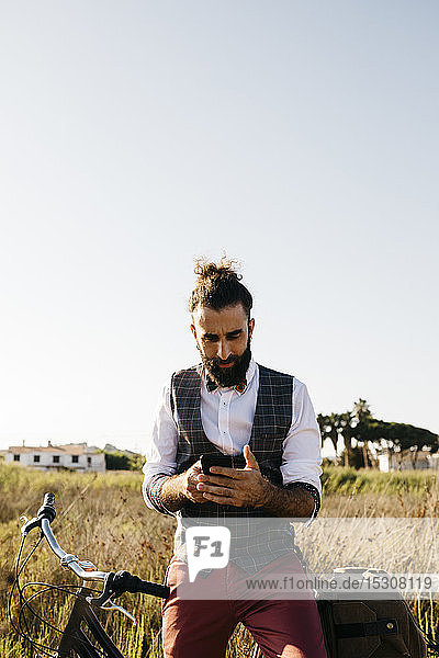 Well dressed man with his bike in the countryside using cell phone