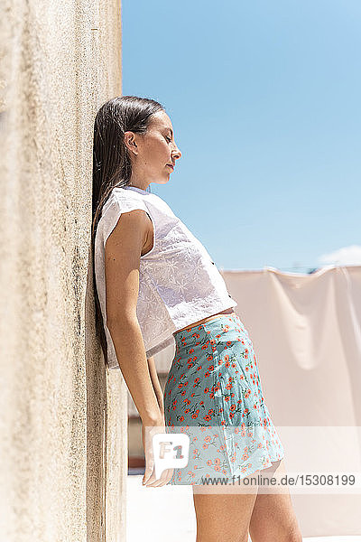 Fashionable young woman with eyes closed leaning at wall