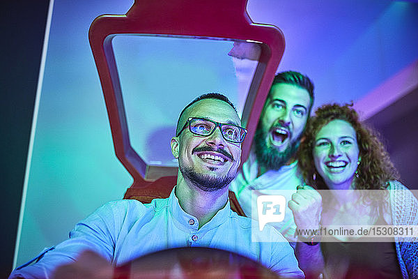 Fröhliche Freunde die mit einem Fahrsimulator in einer Spielhalle spielen und Spaß haben