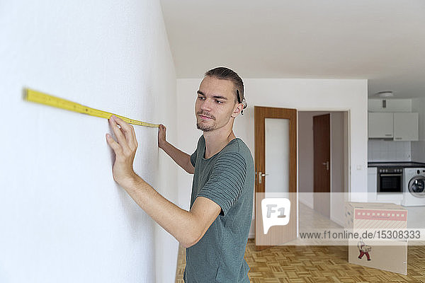 Young man measuring the wall in an empty apartment