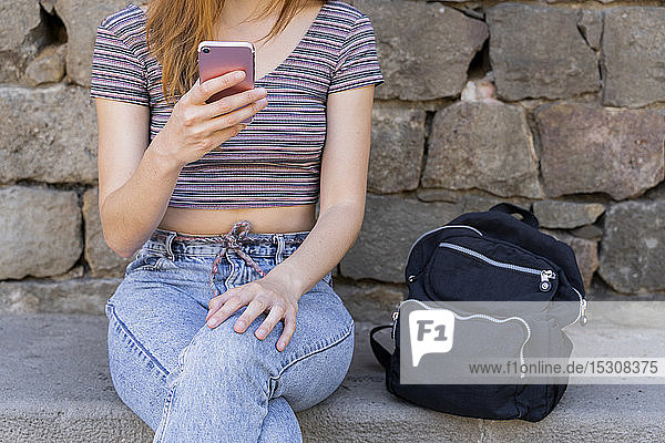 Woman with backpack sitting on a bench unsing cell phone  partial view