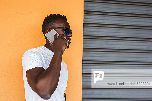 Junger Mann mit weißem T-Shirt und Sonnenbrille telefoniert