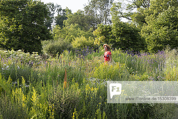 Woman wearing straw hat and red summer dress in garden with wildflowers