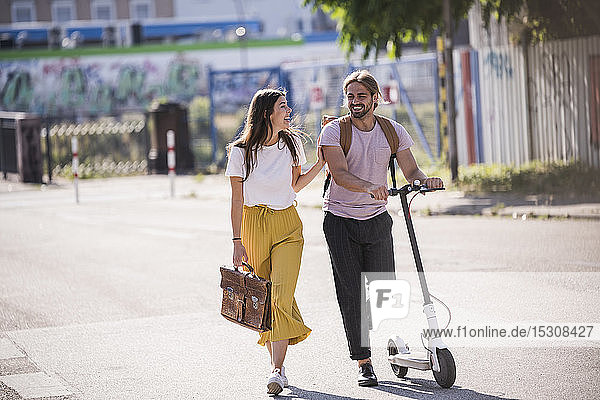 Happy young couple with electric scooter walking on the street