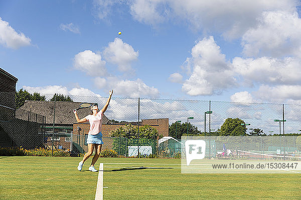 Reife Frau serviert während eines Tennisspiels auf Rasen