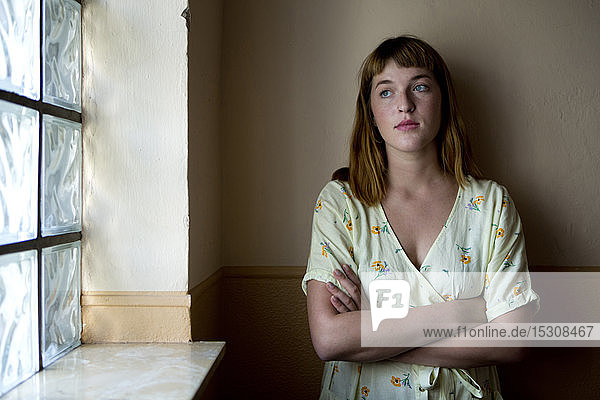 Portrait of serious young woman with arms crossed looking out of window