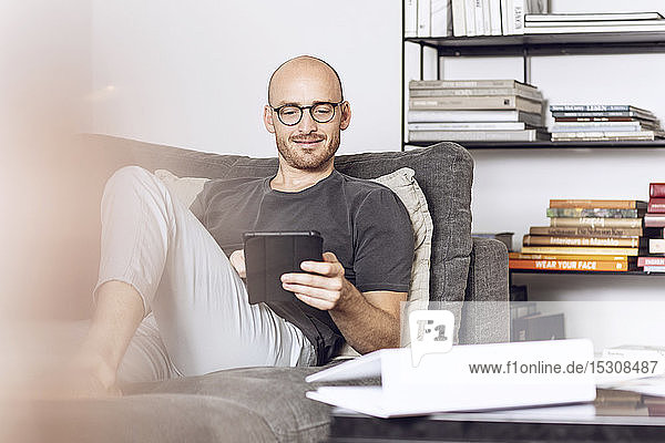 Mann sitzt zu Hause auf einer Couch mit digitalem Tablet