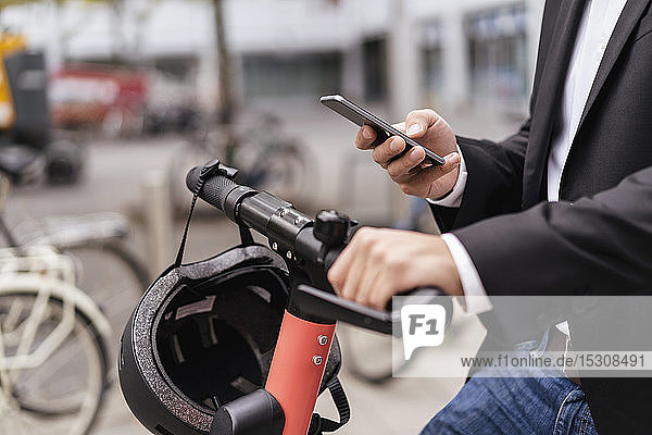 Nahaufnahme eines Geschäftsmannes mit einem E-Scooter  der ein Mobiltelefon in der Stadt benutzt
