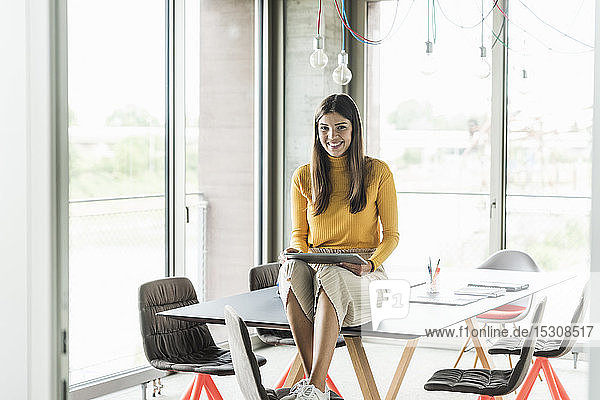 Porträt einer lächelnden jungen Geschäftsfrau mit Tablett im Büro