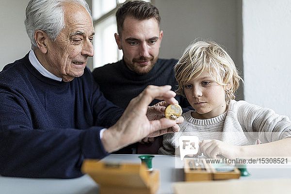 Uhrmacher zeigt einem jungen Mann und Jungen ein Uhrwerk