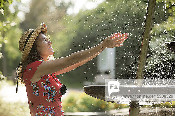 Lächelnde Frau  die im Sommer mit Brunnenwasser spritzt