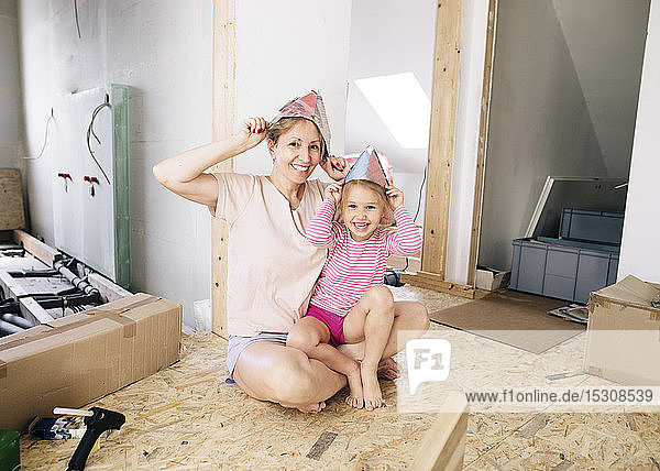 Glückliche Mutter und Tochter mit Papierhüten in einem zu renovierenden Haus