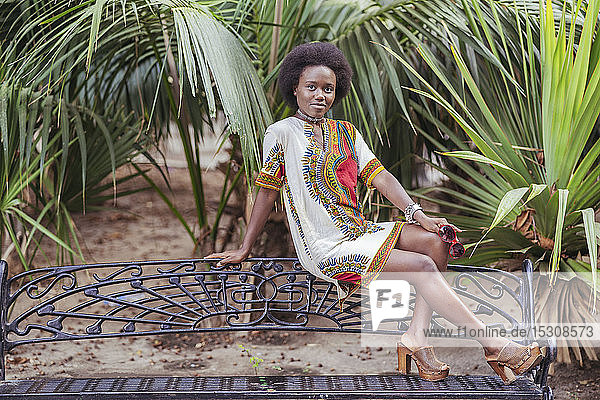 Junge Frau posiert auf einer Bank zwischen tropischen Pflanzen