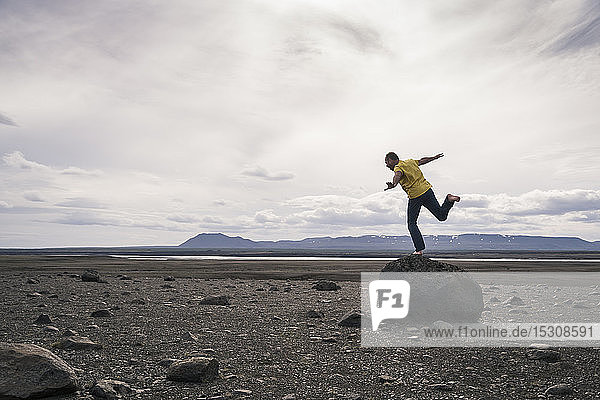 Reifer Mann balanciert auf einem Bein auf einem Felsen im vulkanischen Hochland von Island