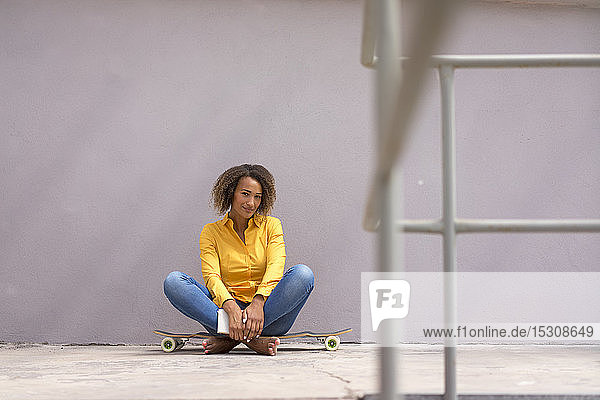 Portrait of young woman book sitting barefoot on skateboard