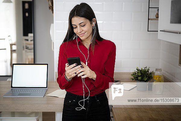 Junge Geschäftsfrau mit Kopfhörern  die zu Hause ein Smartphone benutzt