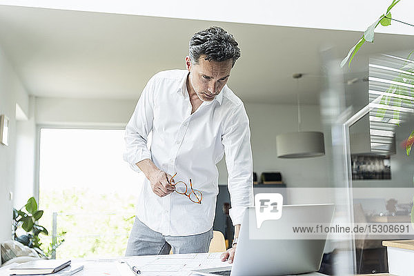 Architect working on blueprint in a bright office using laptop