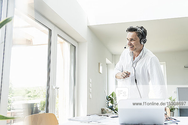Businessman in bright office having conference call using headset and laptop