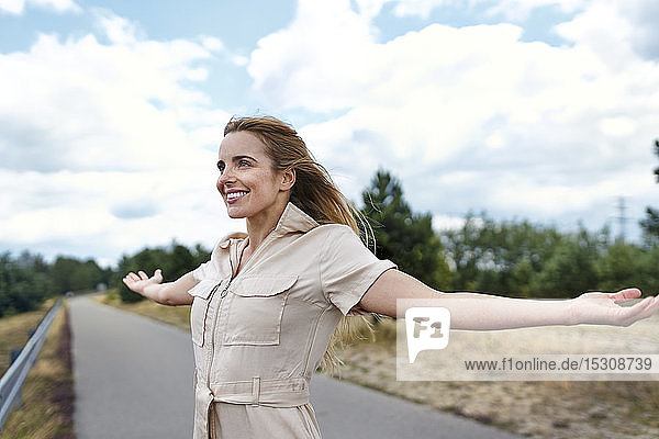 Happy woman standing on a rural road with outstretched arms