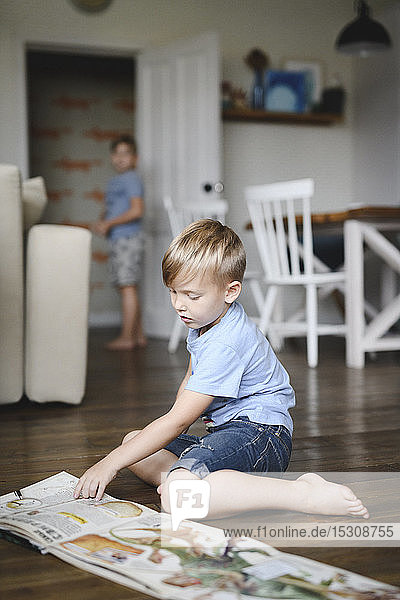 Little boy sitting barefoot on floor in the kitchen watching book