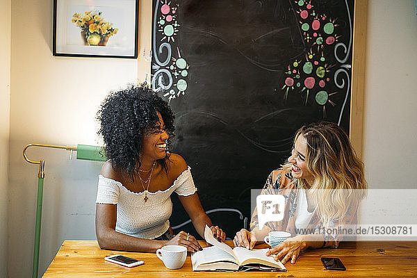 Multikulturelle Frauen  die in einem Café lachen und ein Buch lesen