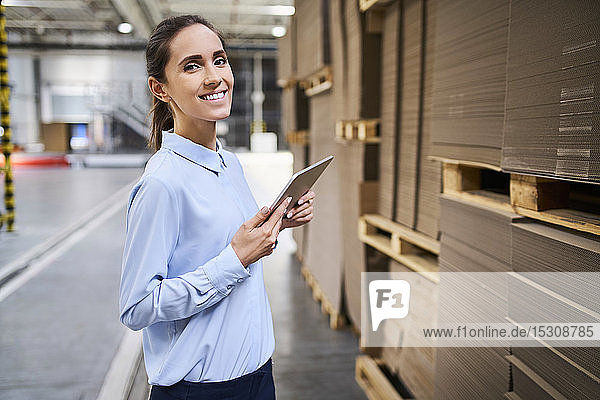 Porträt einer lächelnden Geschäftsfrau mit Tablette in einem Fabriklager