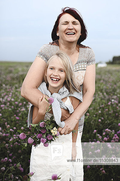 Portrait of laughing grandmother and granddaughter with pickes flowers on a meadow