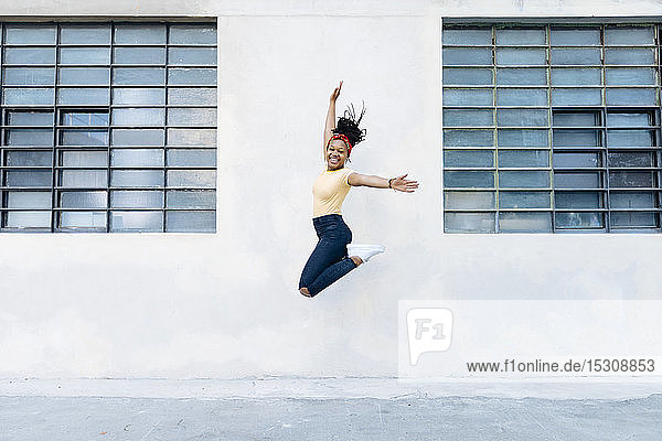 Glückliche junge Frau springt vor weißer Wand in die Luft