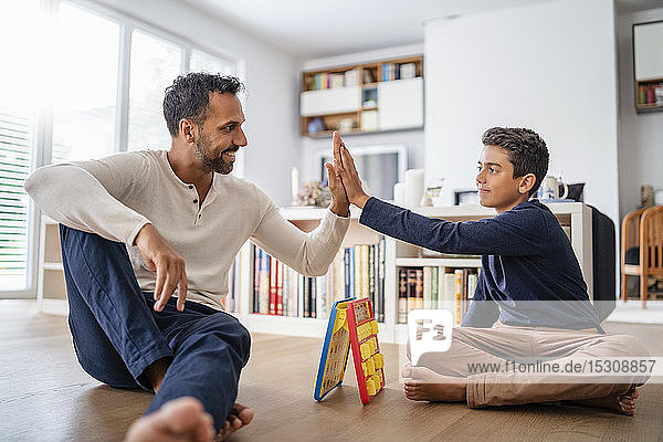 Vater und Sohn sitzen zu Hause auf dem Boden und spielen ein Spiel und High Fiving