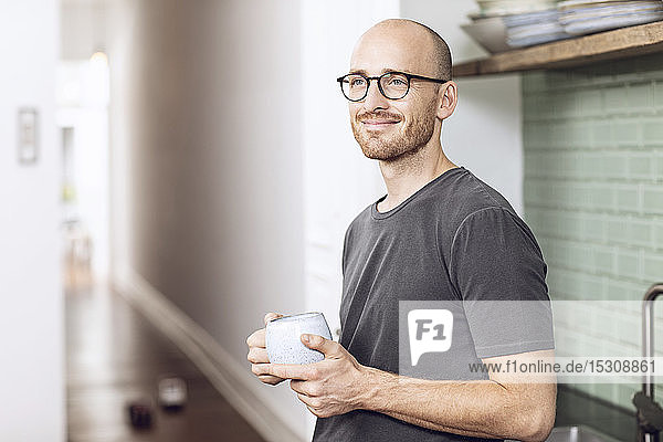 Mann mit einer Tasse  der morgens zu Hause in der Küche steht