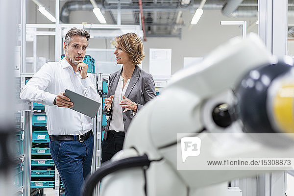 Businesswoman and man with tablet talking at assembly robot in a factory