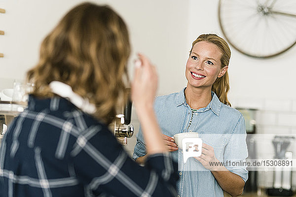 Woman with cup of coffee  talking to customer in a coffee shop