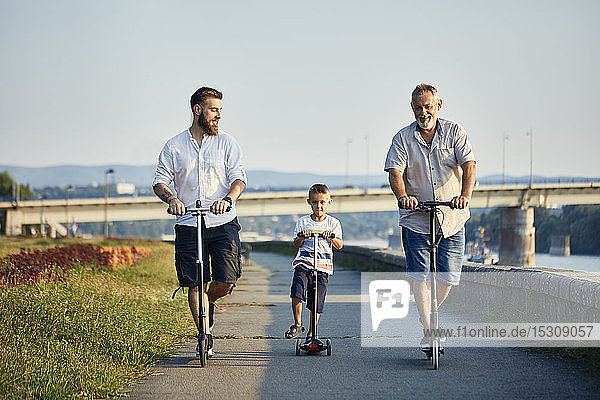 Großvater  Vater und Sohn fahren Roller am Flussufer