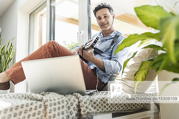 Mature man practising on the guitar using laptop and earphones
