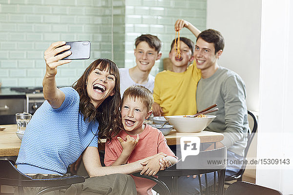 Mother and her four sons taking smartphone selfies at lunch