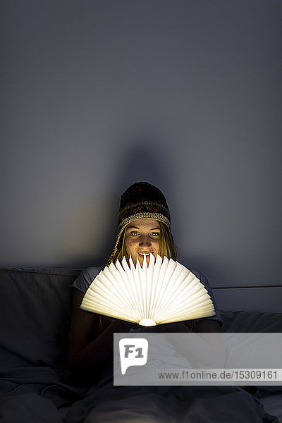 Young woman reading illuminated book in bed at home
