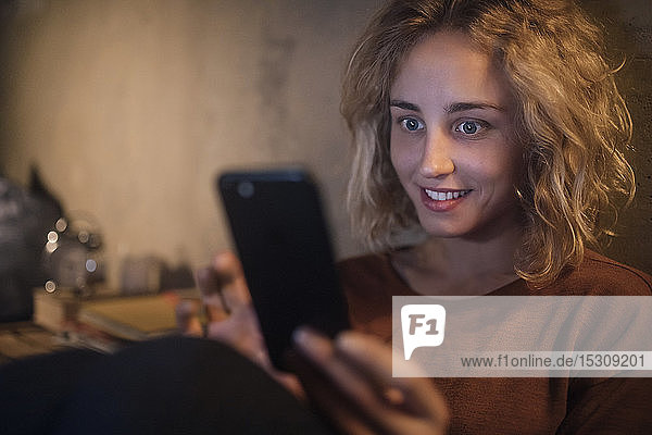 Porträt einer jungen Frau  die zu Hause auf ihr Smartphone starrt