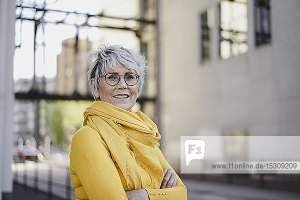Bildnis einer reifen Frau mit grauen Haaren  die eine Brille trägt und gelb gekleidet ist