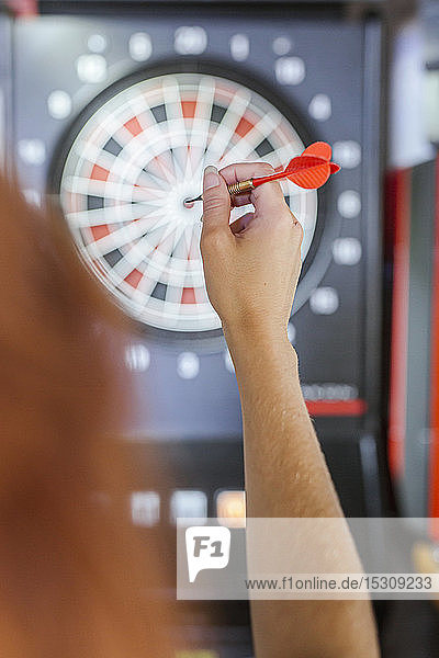 Close-up of woman's hand holding dart in front of dartboard