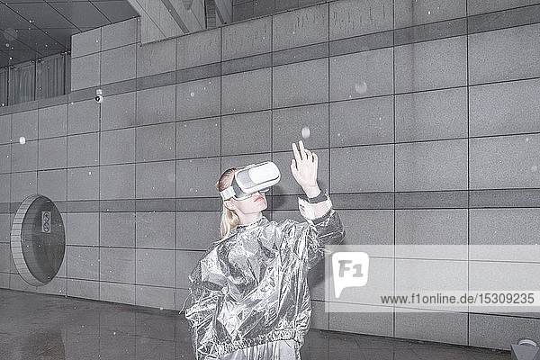Girl in silver suit looking through VR goggles  watching her hand