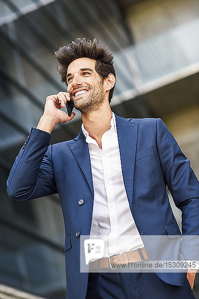 Glücklicher Geschäftsmann telefoniert vor einem Bürogebäude mit seinem Handy